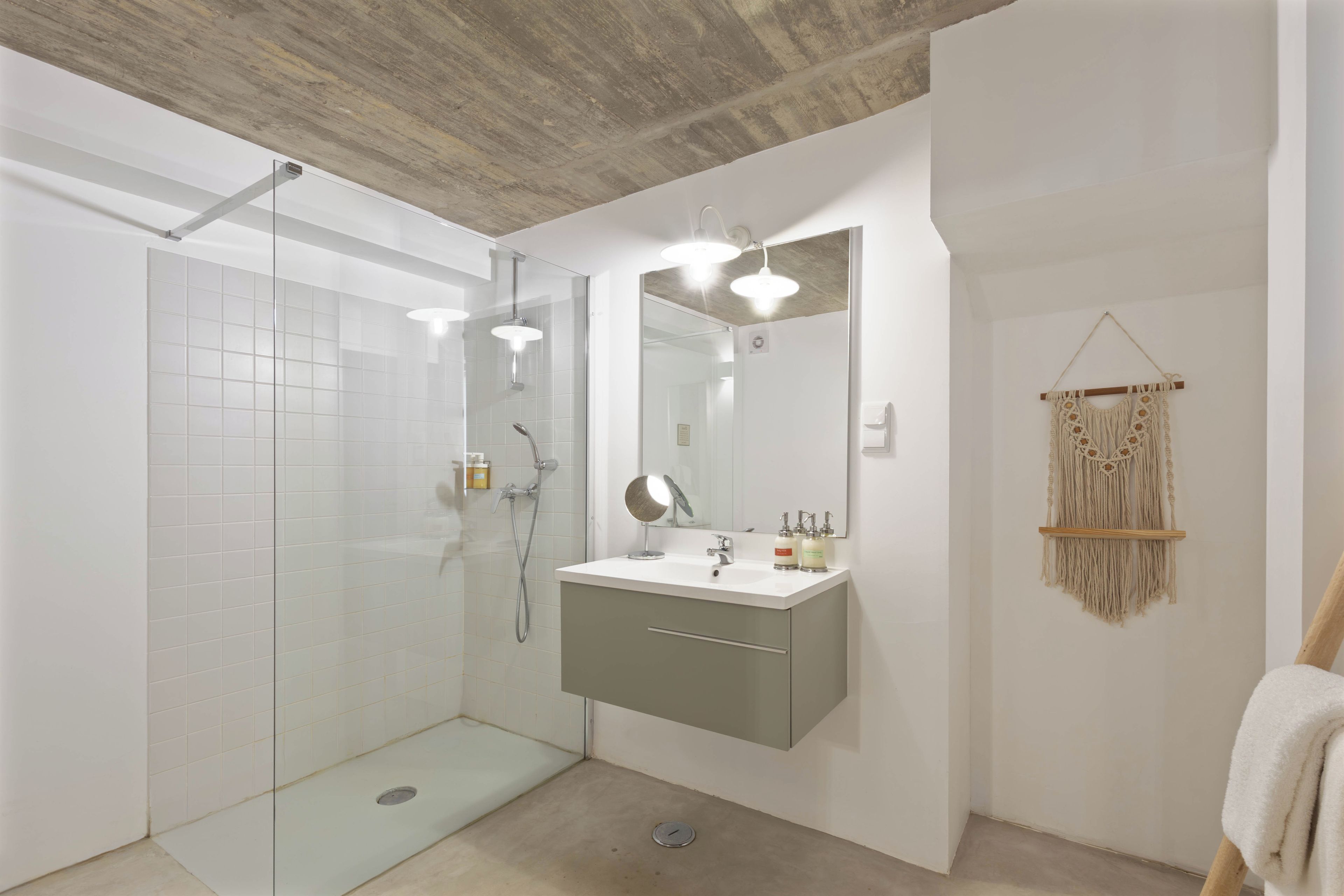 A modern bathroom with a glass-enclosed shower, a vanity with a mirror, and a macrame wall hanging.