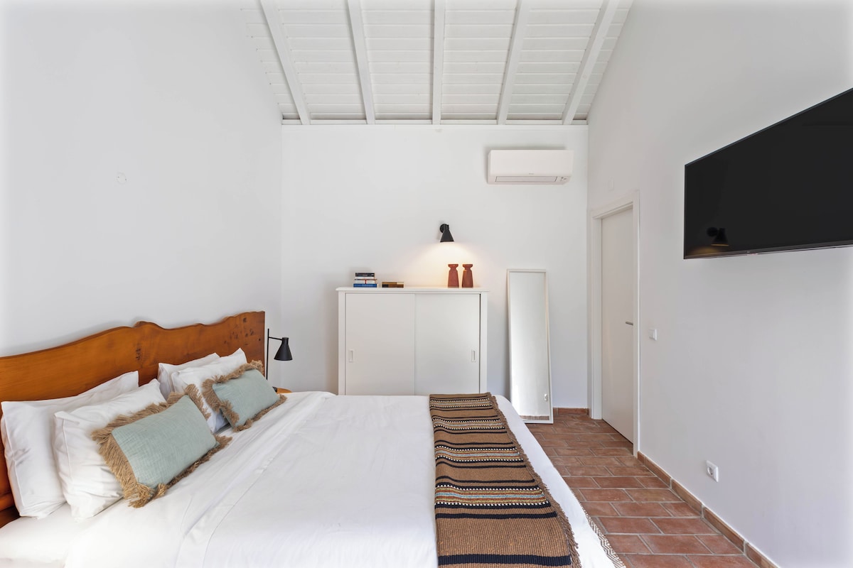 A bedroom with a bed, bedside table, lamp, wardrobe, and a wall-mounted TV.