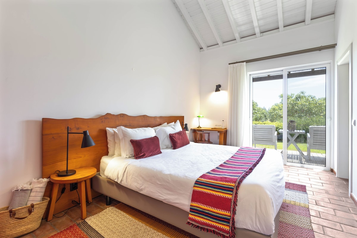 A bedroom with a bed, bedside tables, a lamp, a window, and a view of the outdoors.