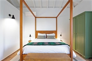 A four-poster bed with white bedding and multiple pillows, a wooden floor, a green wardrobe, and a small wooden table. - Abacatus Farmhouse (Tavira)