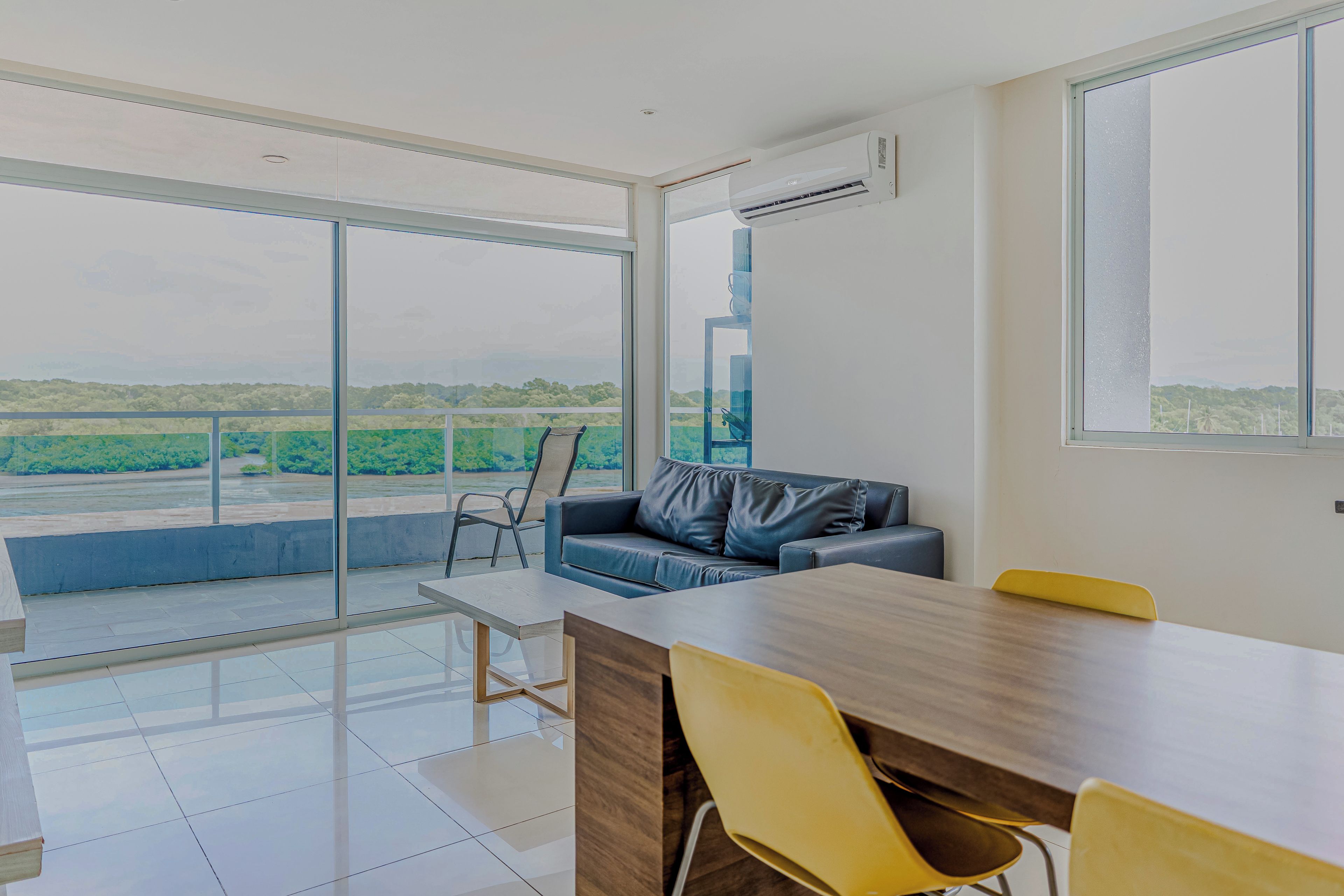 A modern room with a large window, a sofa, a dining table, and chairs.
