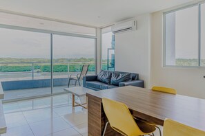 A modern room with a large window, a sofa, a dining table, and chairs. - Ocean Views in El Roble: Pool & Gym Access! (Puntarenas)