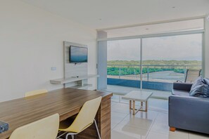 A modern living room with a flat-screen TV mounted on the wall, a dining area with a wooden table and chairs, and a balcony with a view of a green landscape. - Ocean Views in El Roble: Pool & Gym Access! (Puntarenas)
