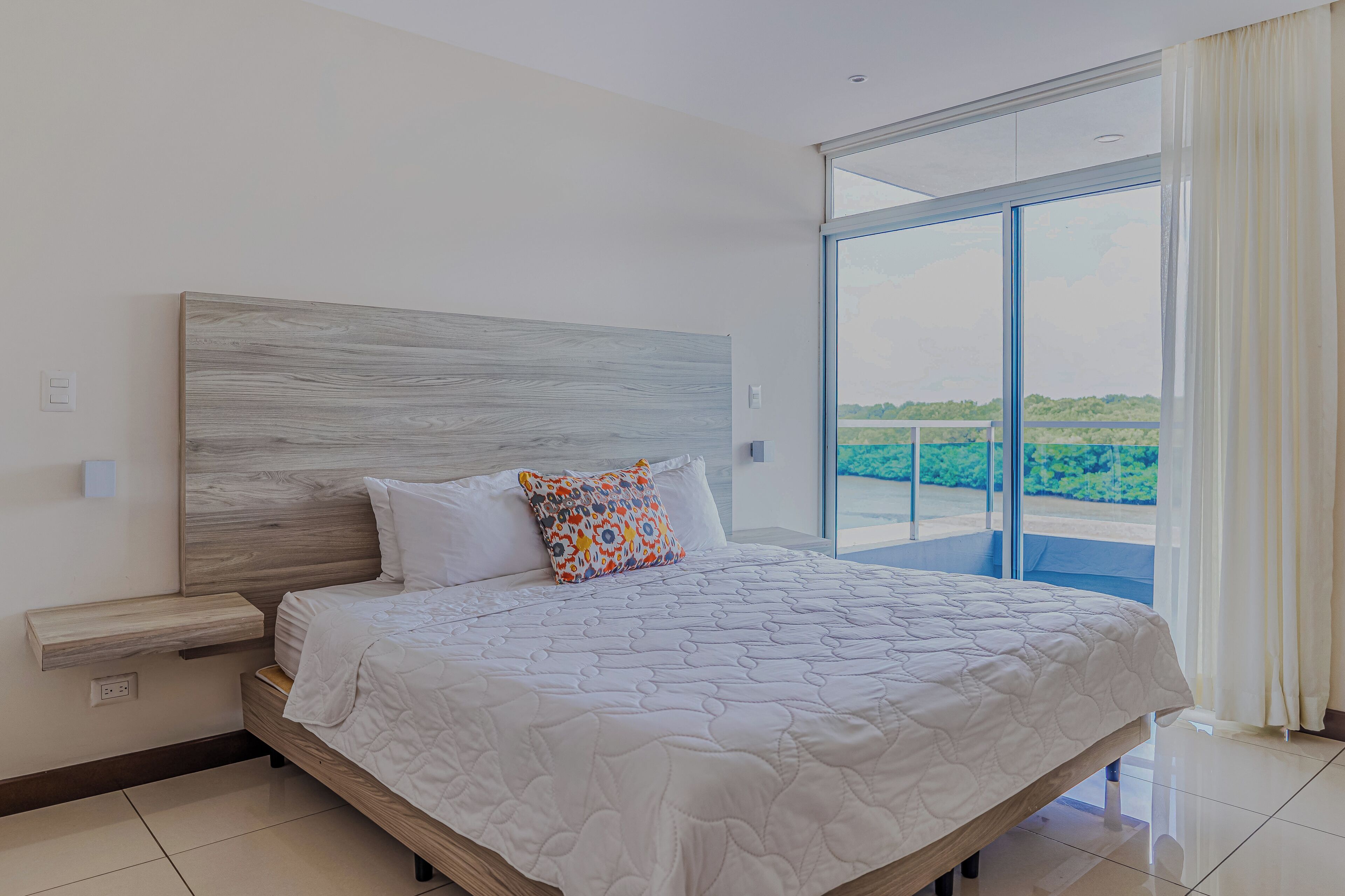 Ein Schlafzimmer mit einem großen Bett, einem hölzernen Kopfteil und Blick durch eine Glastür.