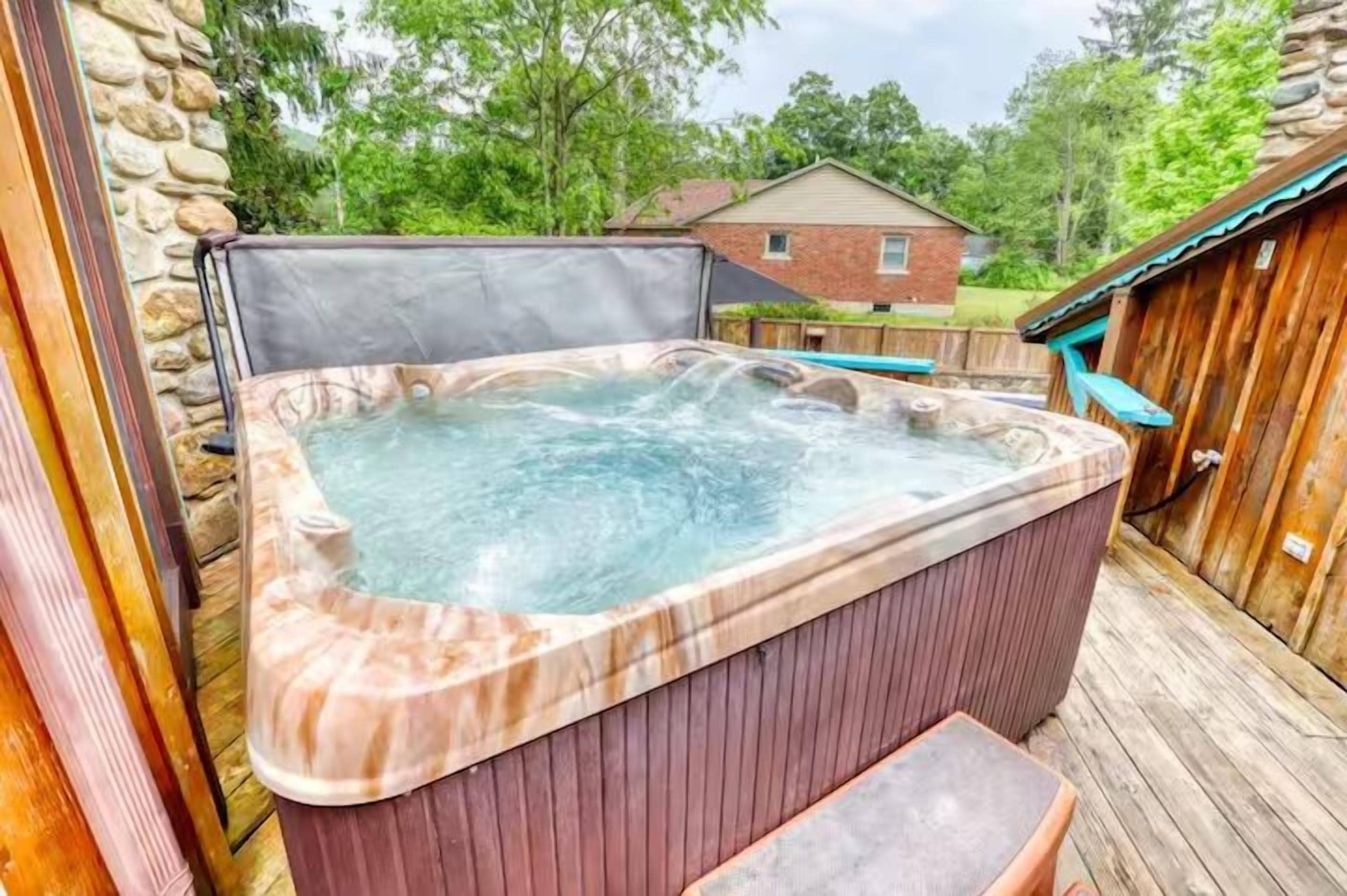 Un bain à remous installé à l’extérieur, avec une terrasse en bois et un mur en pierre.