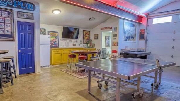 A room with a ping pong table, a blue door, and a yellow cabinet. - Large Ski Home: Seasonal Pool & Year-round Hot Tub (Ellicottville)