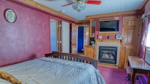 A bedroom with a bed, a fireplace, a television, and a ceiling fan. - Large Ski Home: Seasonal Pool & Year-round Hot Tub (Ellicottville)