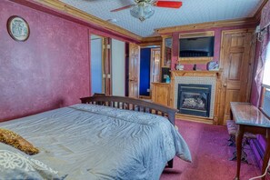 Quarto com cama, lareira, televisão e ventoinha de teto.