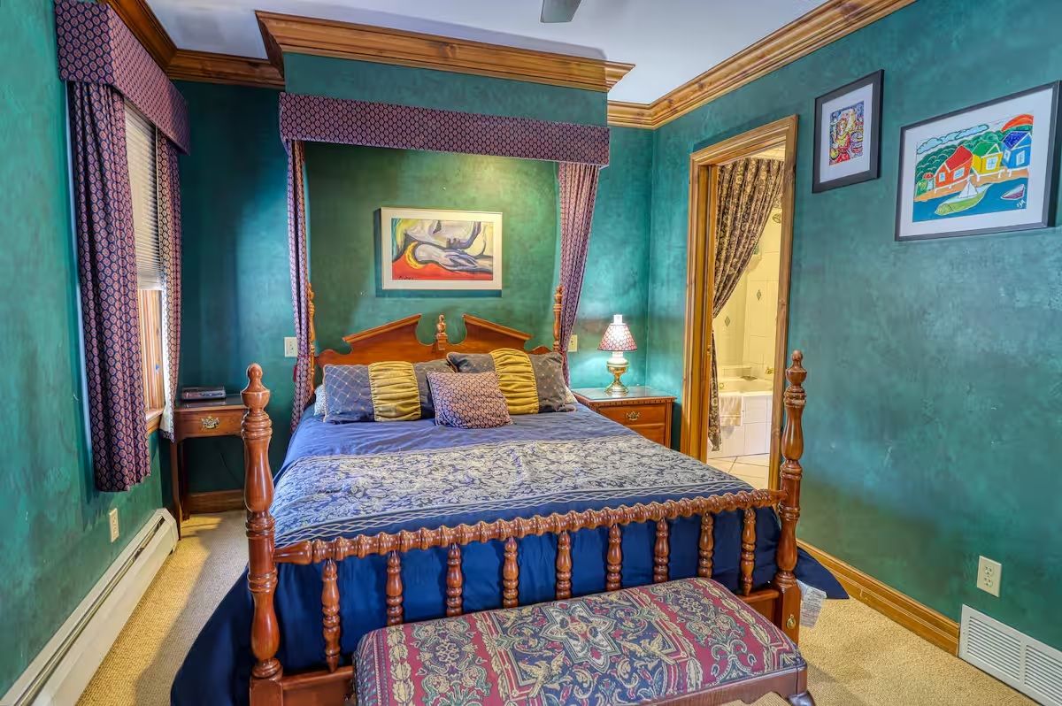 A bedroom with a four-poster bed, a nightstand, a lamp, and a window with curtains.