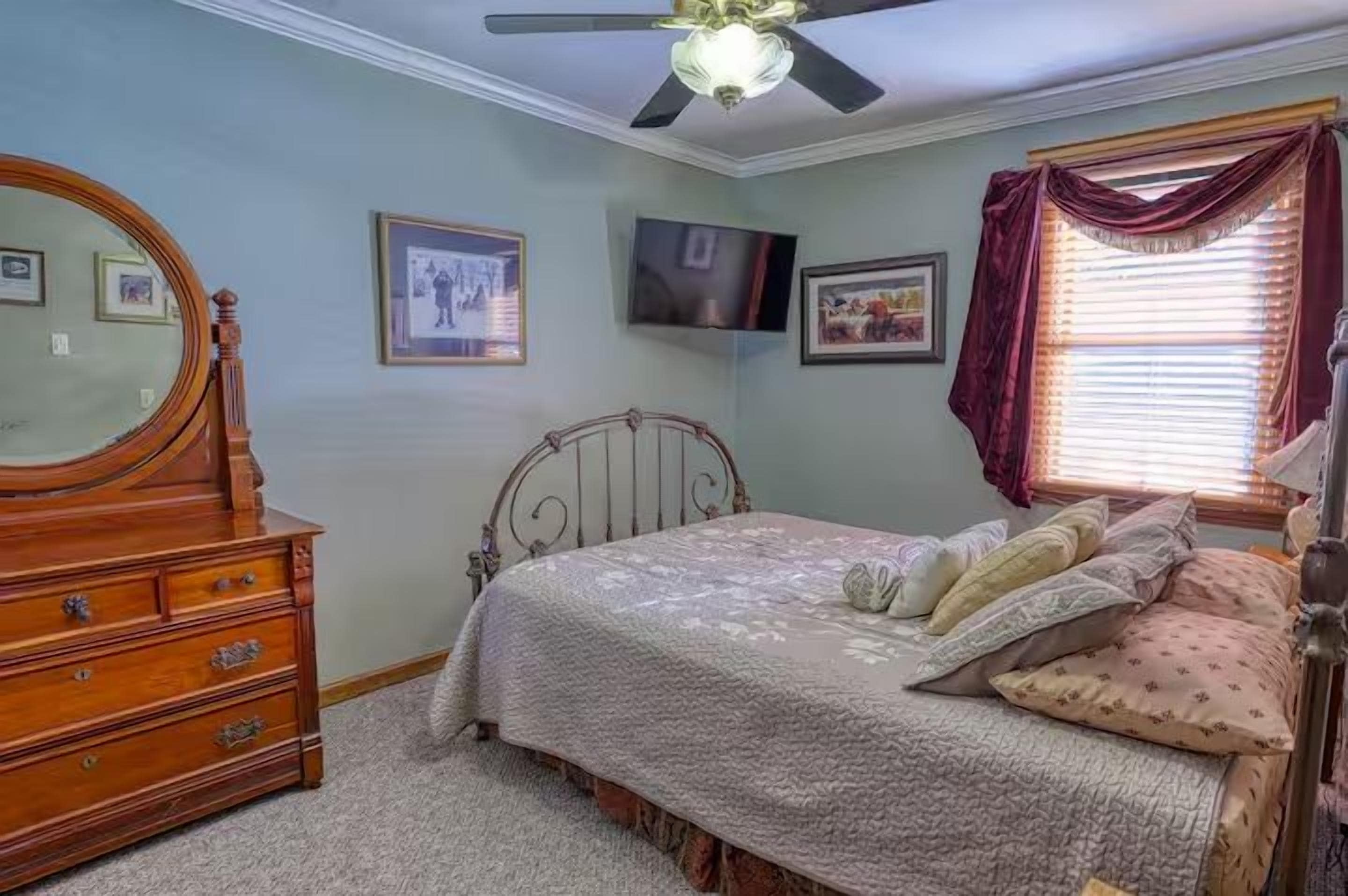 A bedroom with a bed, dresser, ceiling fan, and framed pictures on the wall.