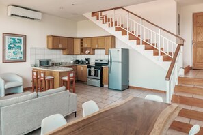 Cozinha moderna com armários de madeira, área de jantar com mesa de madeira e escada com corrimão de madeira.