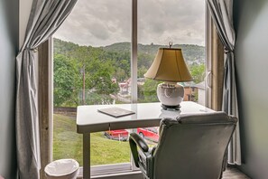A room with a view of a green landscape, a table with a lamp, and a chair.