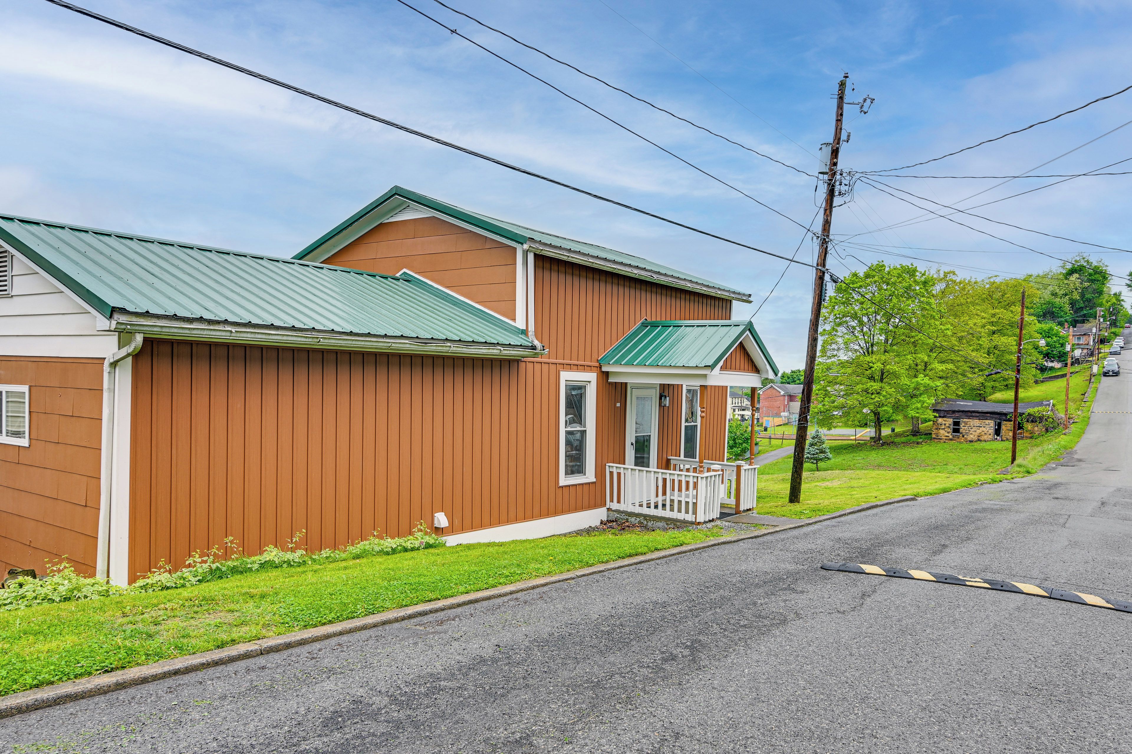 A two-story wooden house with a green roof, a front porch, and a driveway.