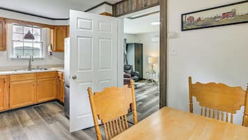 A modern kitchen with wooden cabinets, a dining area with a wooden table and chairs, and a view of a countryside landscape through a window.