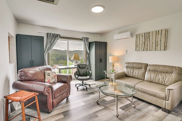 A modern living room with a leather sofa, a glass coffee table, and a view of a green landscape through the window.