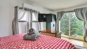 Hotellihuone, jossa on sänky, taulutelevisio, puinen yöpöytä ja näkymä ulos.