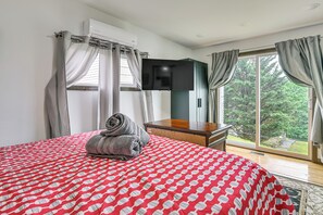 A hotel room with a bed, a flat-screen TV, a wooden nightstand, and a view of the outdoors.