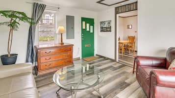A living room with a glass coffee table, leather sofa, wooden dresser, and a potted plant.
