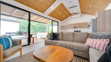 A modern living room with a wooden ceiling, a sofa set, a coffee table, and a view of a pool outside.
