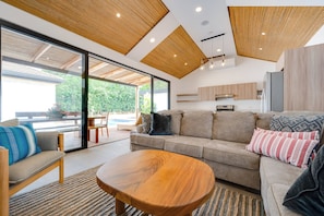 A modern living room with a wooden ceiling, a sofa set, a coffee table, and a view of a pool outside. - Pool, Walkable Location! Luxe Tamarindo 4BR Home (Tamarindo)