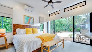 Camera da letto moderna con un letto grande, una ventola a soffitto e vista su un giardino attraverso ampie finestre.