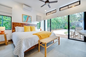 A modern bedroom with a large bed, a ceiling fan, and a view of a garden through large windows.