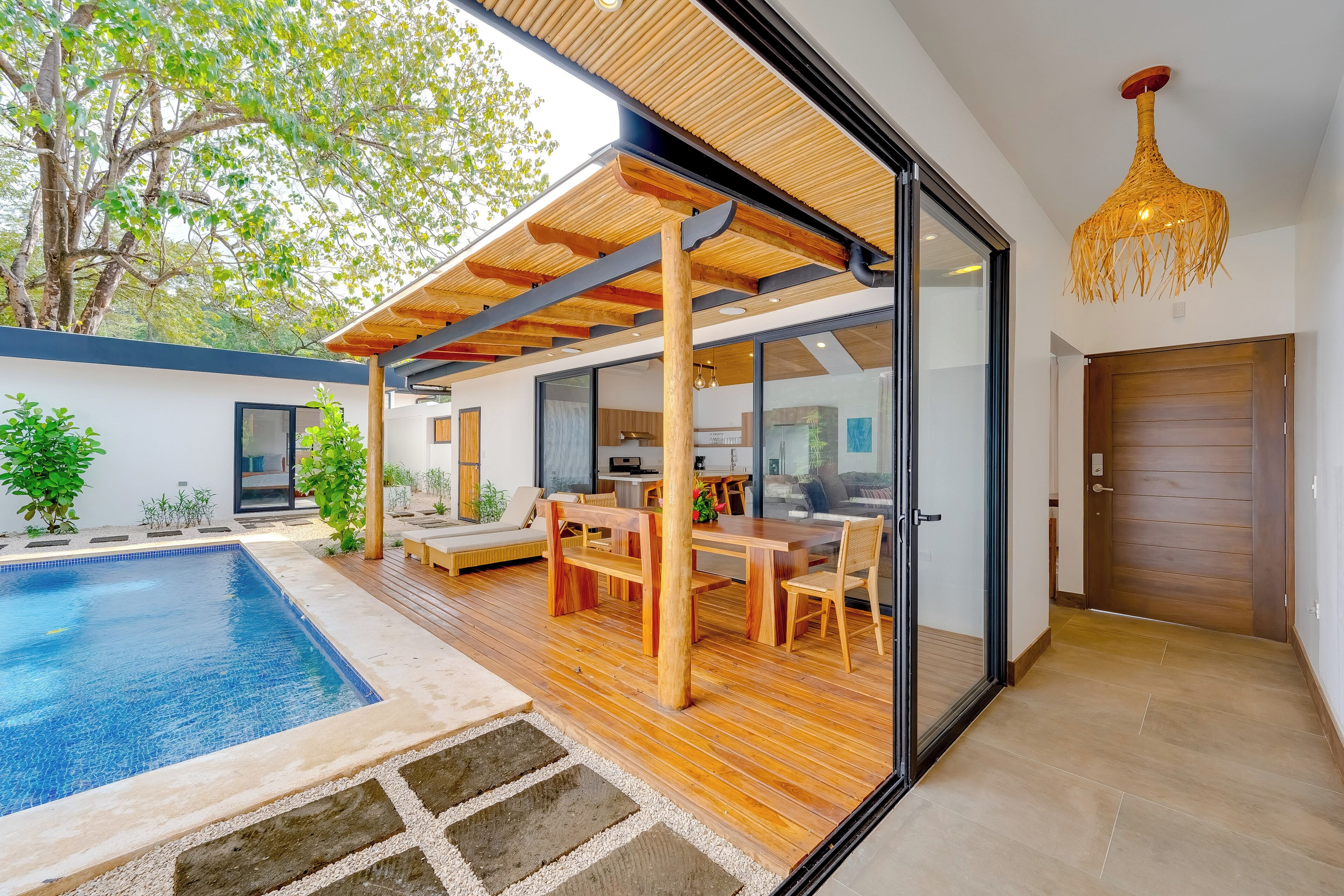 Une maison moderne dotée d’une piscine, d’une terrasse en bois et de portes vitrées donnant sur un espace repas.