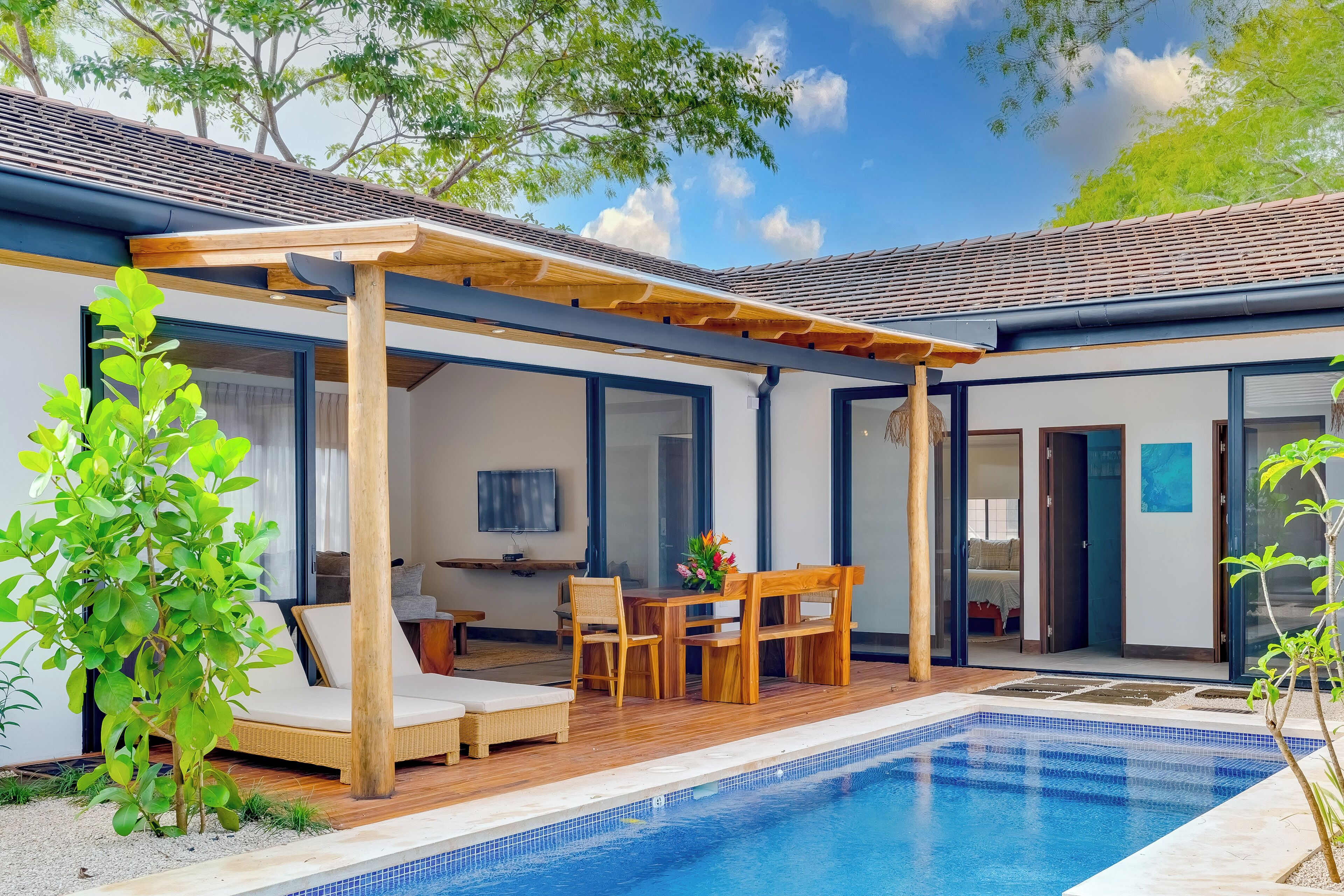 A modern outdoor pool area with a pergola, lounge chairs, and a dining table.