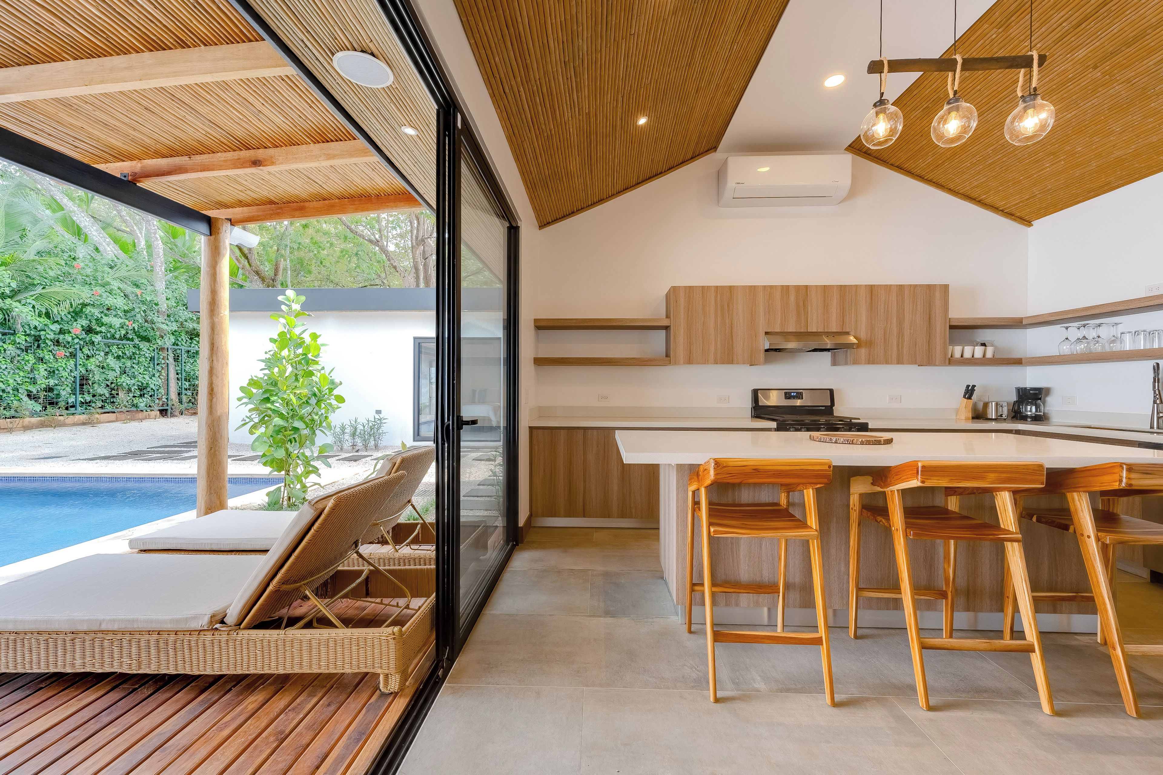 A modern kitchen with a large island, wooden bar stools, and a view of a swimming pool.