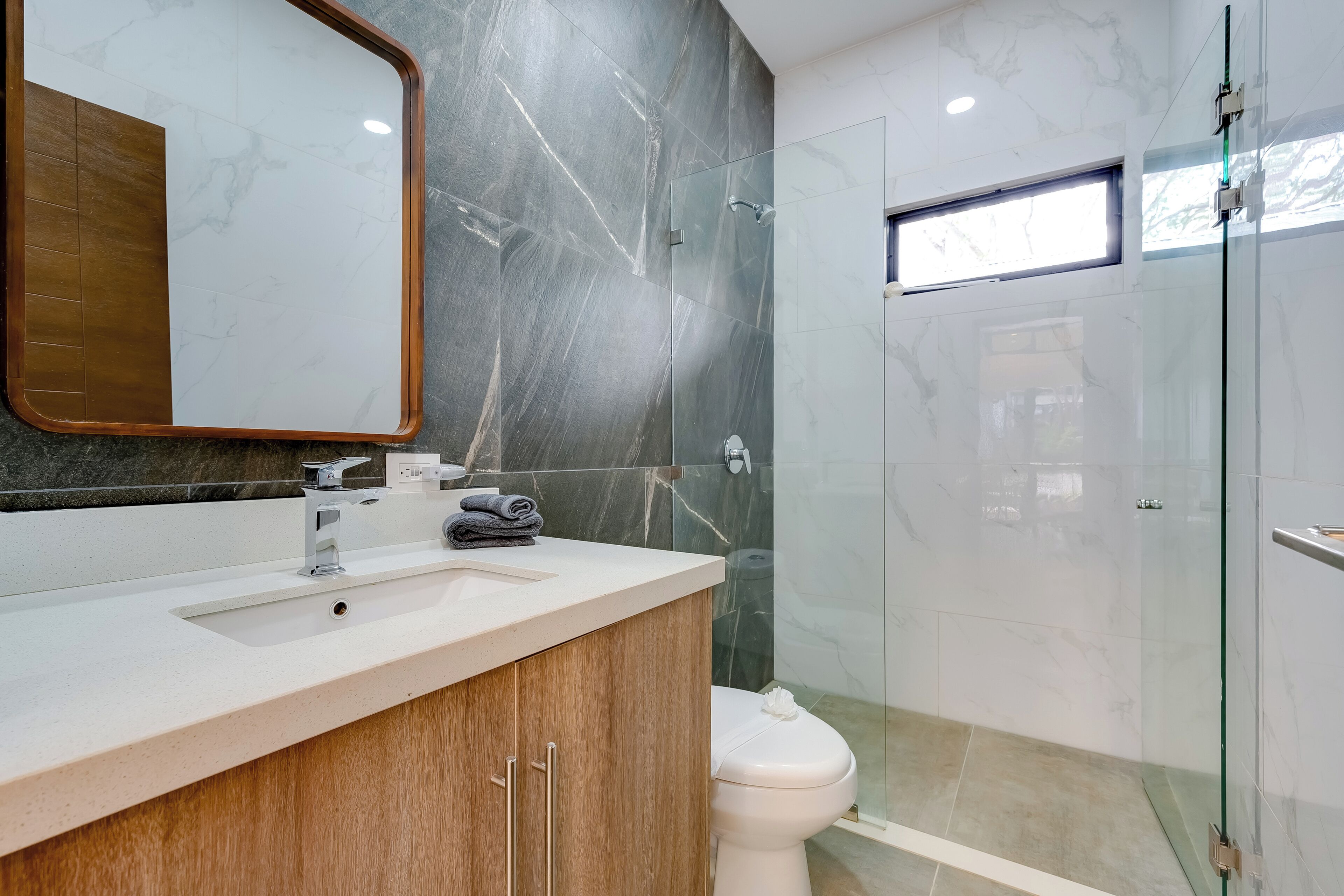 A modern bathroom with a marble vanity, a toilet, and a glass-enclosed shower area.