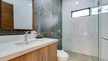 A modern bathroom with a marble vanity, a toilet, and a glass-enclosed shower area.