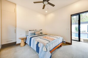A bedroom with a bed, a ceiling fan, a small wooden table, and a view of a swimming pool through a glass door. - Pool, Walkable Location! Luxe Tamarindo 4BR Home (Tamarindo)