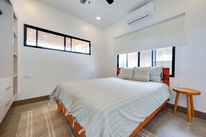 A bedroom with a bed, a bedside table, a window, and an air conditioning unit.