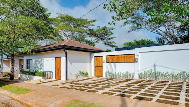 Una casa moderna con tetto in tegole, un giardino anteriore con area pavimentata e un muro bianco con porta in legno.