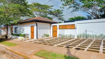 A modern house with a tiled roof, a front garden with a paved area, and a white wall with a wooden door.