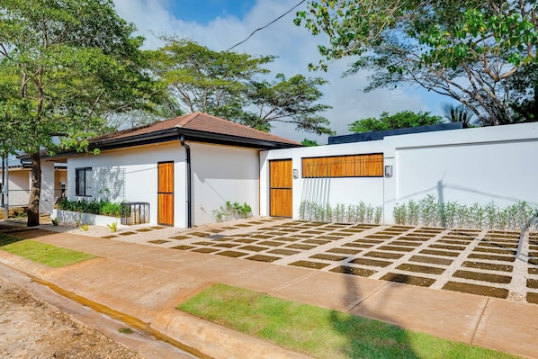 A modern house with a tiled roof, a front garden with a paved area, and a white wall with a wooden door.
