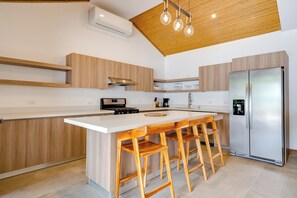 A modern kitchen with a central island, wooden bar stools, a stainless steel refrigerator, and a wooden ceiling. - Pool, Walkable Location! Luxe Tamarindo 4BR Home (Tamarindo)