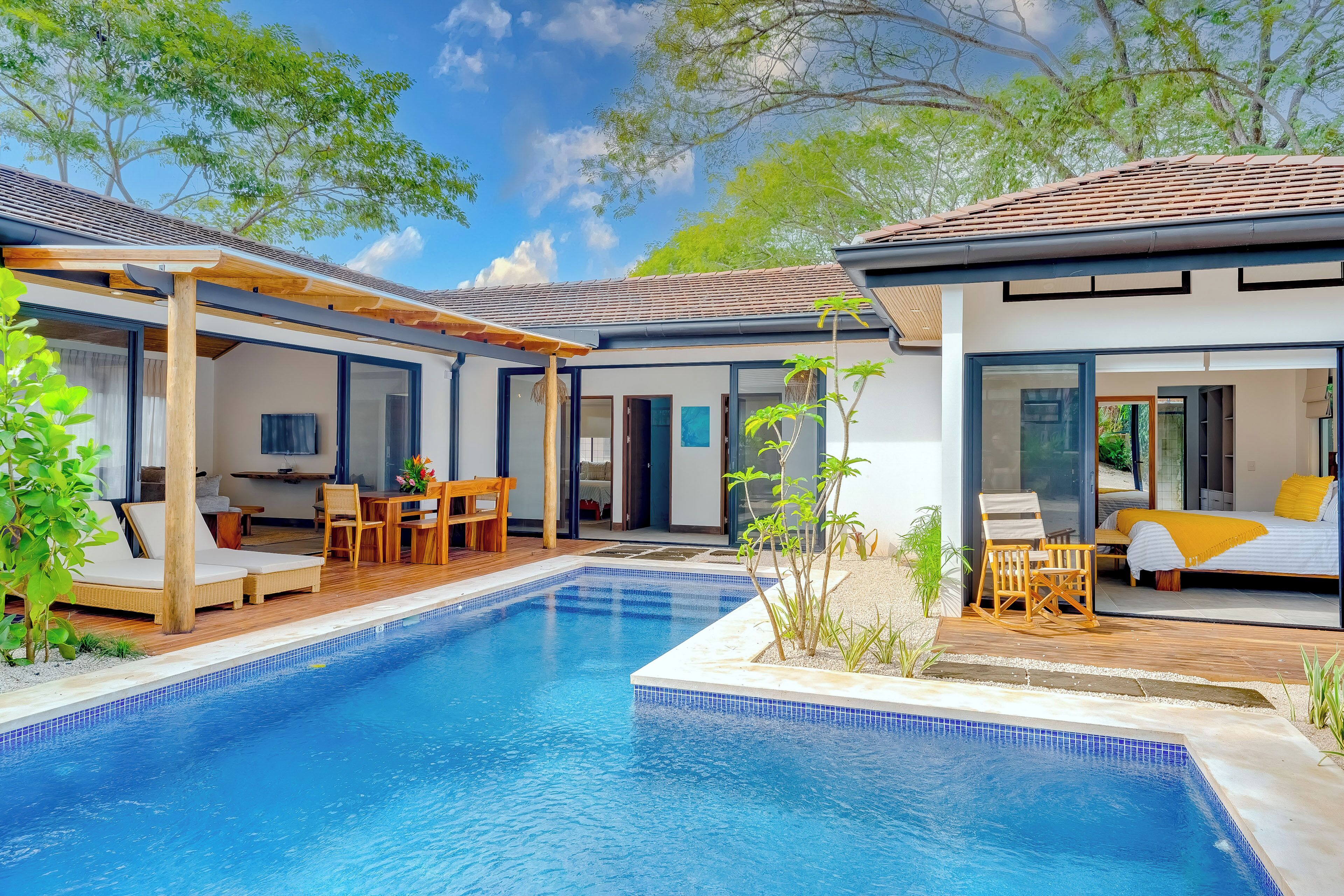 A modern outdoor pool area with a pergola, lounge chairs, and a dining set.