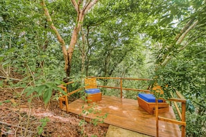 A wooden deck with two blue cushioned chairs, surrounded by dense green foliage. - Walk to Flamingo Beach: 2-unit Base w/ Ocean Views (Cabo Velas)