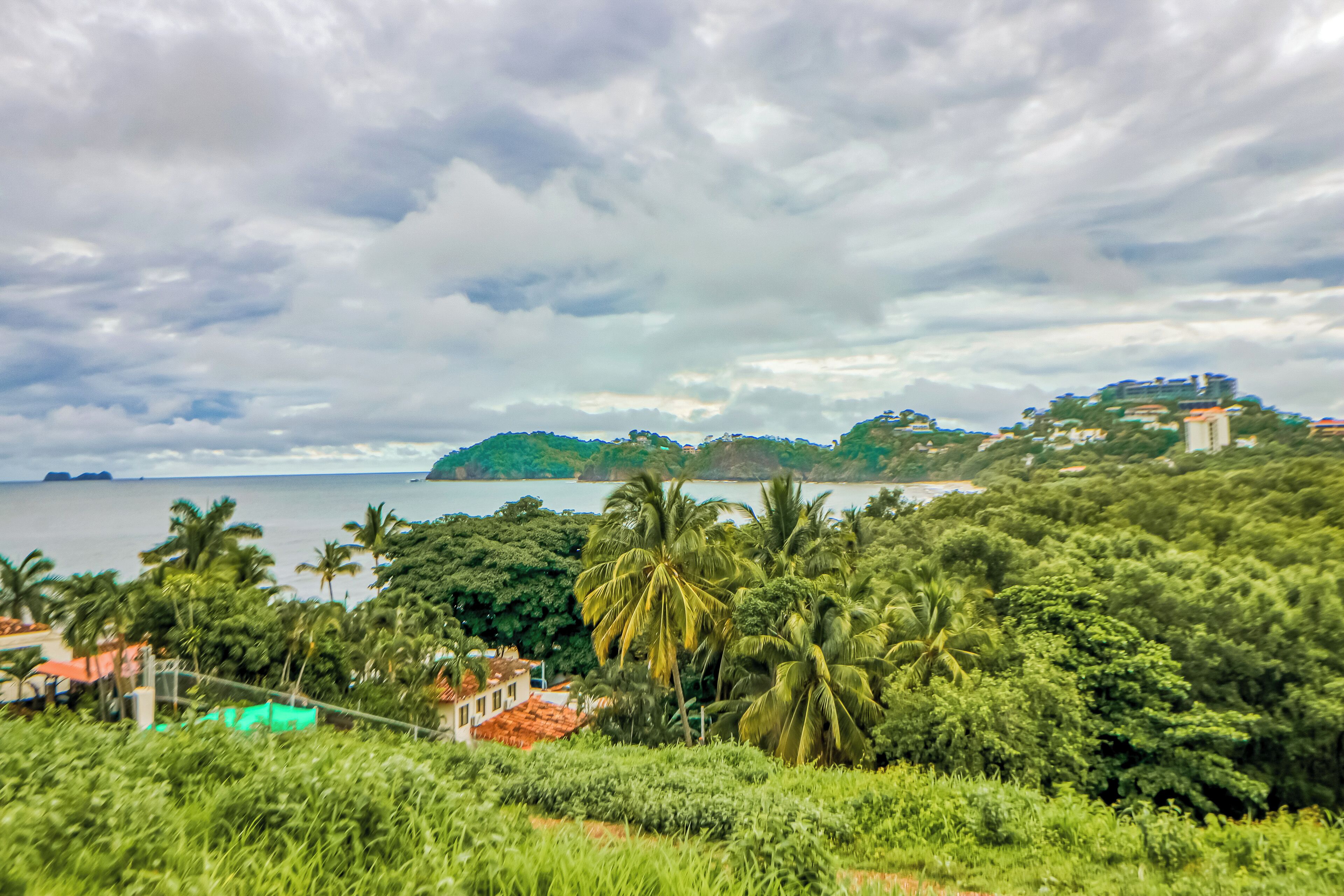 A coastal landscape with dense greenery, a body of water, and distant hills.
