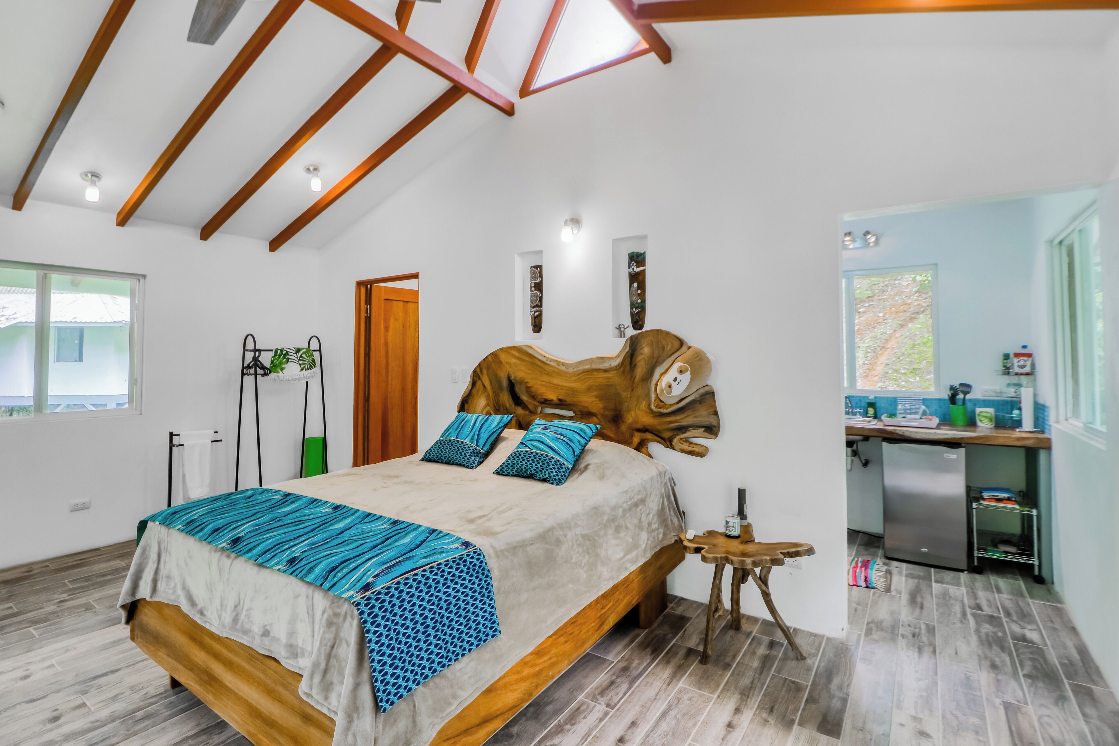 Ein Schlafzimmer mit schrägemaßten Wänden, einem Bett mit gemusterten Textilien, einem Holzkopfende und einem kleinen Holzschemel.