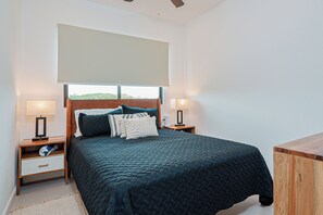 Une chambre à coucher comprenant un lit, deux tables de chevet, une commode, une fenêtre avec vue et un ventilateur de plafond.