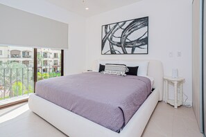 Ein Schlafzimmer mit einem großen Bett, einem Nachttisch, einem Wandbild und Blick ins Freie.