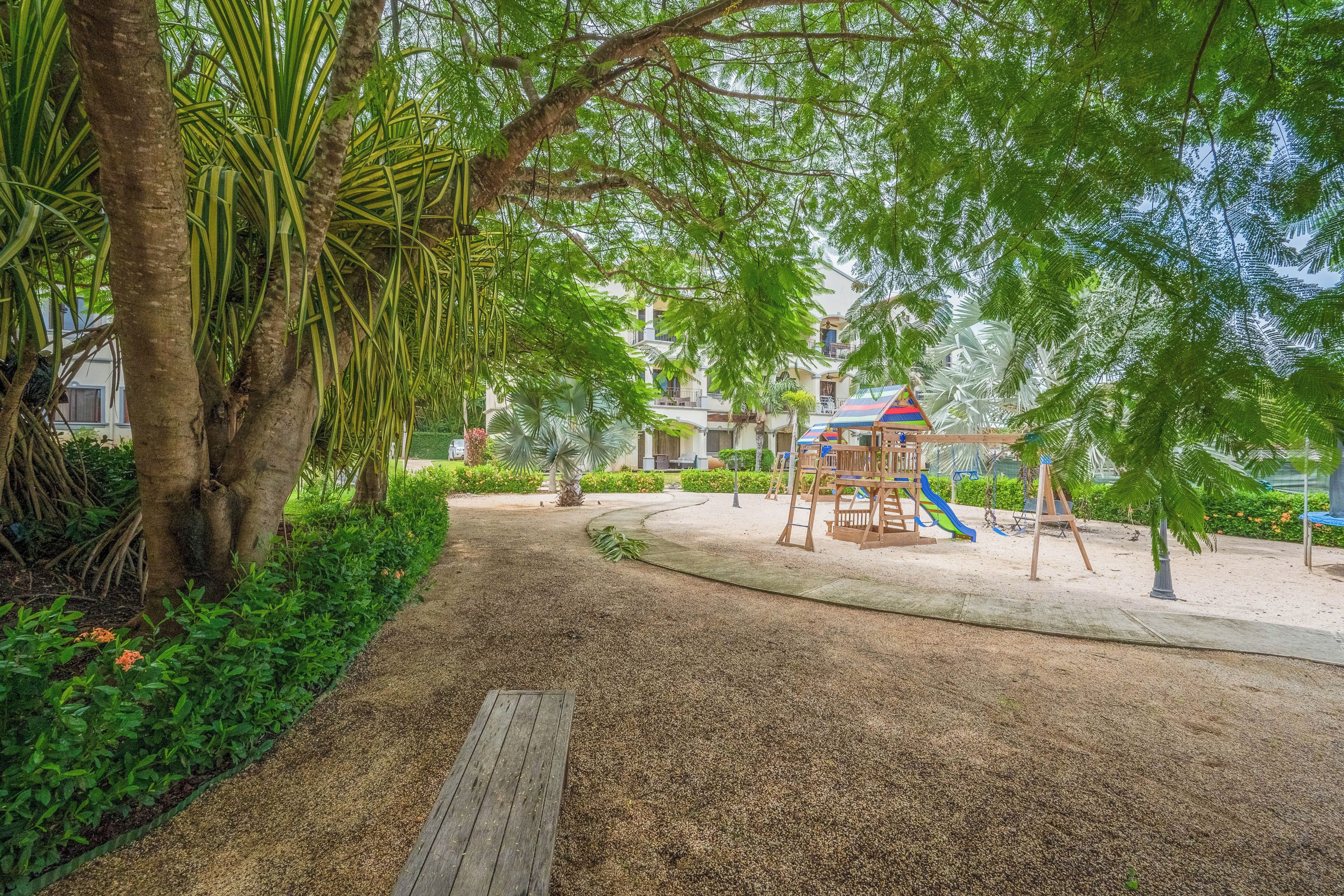 Une aire de jeux avec un toboggan et des structures d’escalade, entourée d’arbres et bordée d’un sentier.
