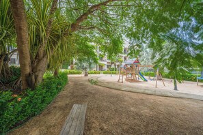 Ein Spielplatz mit Rutsche und Klettergerüsten, umgeben von Bäumen und einem Weg.