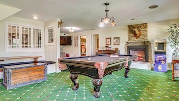 A billiards room with a pool table, a fireplace, and a vintage arcade machine.