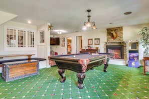 Uma sala de jogos com mesa de bilhar, lareira e máquina de fliperama antiga.