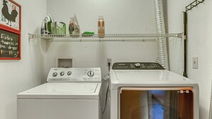 A laundry area with a front-loading washer and dryer, a shelf with various items, and a wall-mounted rack. - Hot Tub Ski Home: Rooster's Den in Ellicottville (Ellicottville)