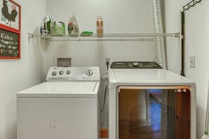 A laundry area with a front-loading washer and dryer, a shelf with various items, and a wall-mounted rack. - Hot Tub Ski Home: Rooster's Den in Ellicottville (Ellicottville)
