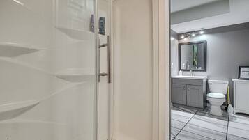 A bathroom with a white toilet, a sink, and a mirror above it. There is a cabinet with a door and a shower area visible.